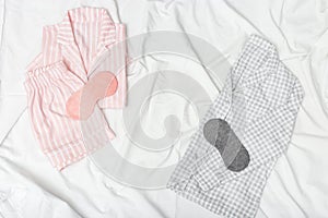 Pink and grey pajamas and eye mask on white sheet on bed. Night suit for peaceful sleeping