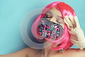 Pink hair posing in a studio in a mask of flowers and gloves, this spring`s fashion. Pandemic, coronavirus, spring. Portrait