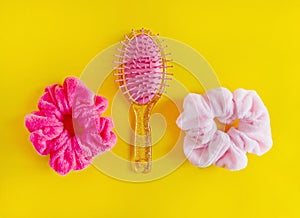 Pink Hair scrunchies and hairbrush on yellow background, beauty concept.