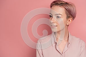 Pink-haired young woman looks somewhere away with quiet smile, pink background