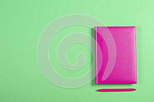 Pink hardcover book and pen on green background