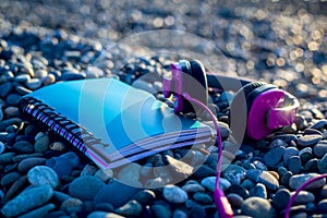 Pink headphones lying at paper notebook on sea beach