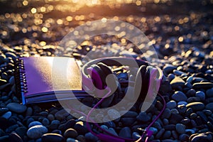 Pink headphones and paper notebook lying on sea beach