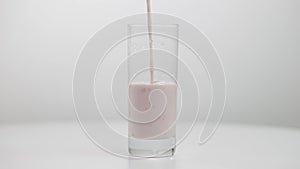 Pink healthful fruit yogurt pouring in transparent glass close-up. Healthy dairy milk product pours in container at