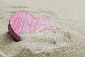 Pink heart made of wood in the sand of a beach, love concept