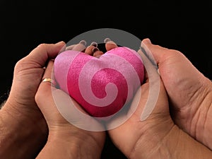 Pink heart on the palms of a woman and a man. Two pairs of hands hold a heart, on a black background. Concept: take care of love,