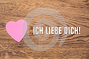 Pink heart post-it with the text `Ich liebe dich`on a wooden background. Translation: `I love you`