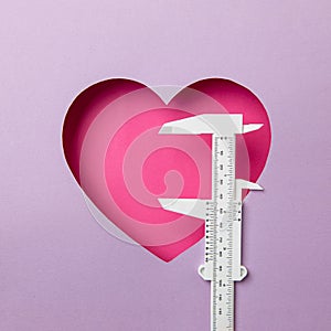 Pink heart on a purple background. At the heart is a white micro meter. Concept measuring love. Copy space