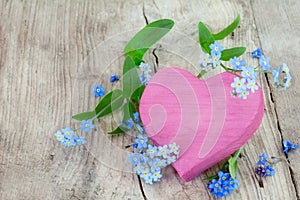 pink heart shape made of wood with forget-me-not flowers on a wooden background