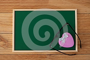 The pink heart-shaped box is decorated with ribbon and black eyeglasses on a green chalkboard.