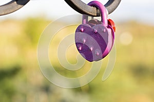 Pink heart shaped lock hangs from bridge chain, wedding custom is symbol of eternal love