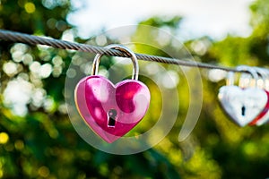 The pink heart shaped love padlock is hanging on wire in blur background