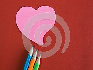 Pink heart-shaped memorandum on red paper with colorful pencils