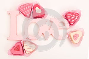 Pink heart shaped petit fours cakes seen from above decorated around pink letters stating Love photo