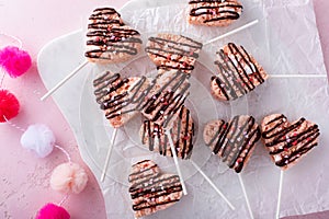 Pink heart shaped rice krispie treats drizzled with dark chocolate on a marble board