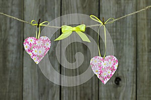 Pink hearts and yellow ribbon hanging on clothesline by rustic wooden background