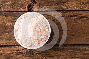 Pink Himalayan salt in bowl on rustic wooden table.