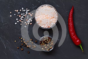 Pink Himalayan salt and mix of peppers in a glasses bowls on the black background.