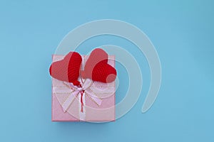 pink holiday box with two red knitted heart shaped balls on blue background