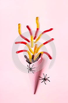 Pink ice cream cone with colorful marmalade worms and spiders. Minimal halloween composition