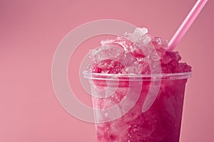 a pink iced slushie in a plastic cup with a straw on a plain studio background