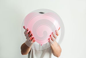 Pink inflatable heart-shaped balloon in hand. White background