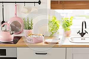 Pink kettle and cake on wooden countertop in bright kitchen inte