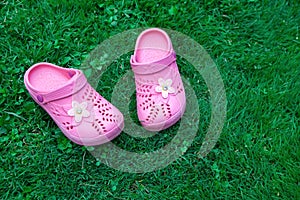 Pink kid`s slippers on green lawn. Copy space. Top view, located at side of frame. Horizontal. Concept of unity with nature.