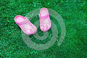 Pink kid`s slippers on green lawn. Copy space. Top view, located at side of frame. Horizontal. Concept of unity with nature.