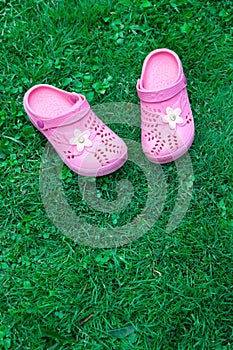 Pink kid`s slippers on green lawn. Top view, located on top of the frame. Vertical. Concept of unity with nature.