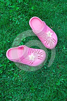 Pink kid`s slippers on green lawn. Top view, in the middle of frame. Vertical. Concept of vacation with children.