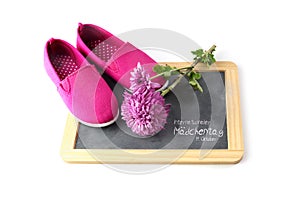 Pink kid shoes and a flower on a writing blackboard isolated on