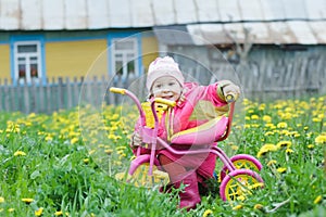 Pink kids trike with yellow wheels and little hunkering toddler girl sitting behind vehicle