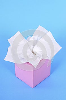 Pink kleenex style tissue box, plain blue background, copy space, vertical