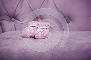 Pink knitted baby booties closeup standing on the couch