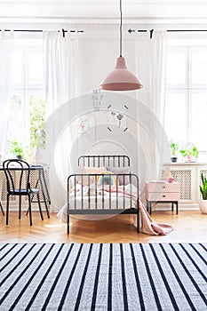 Pink lamp above striped carpet in girl`s room interior