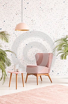 Pink lamp above wooden table and armchair in pastel living room