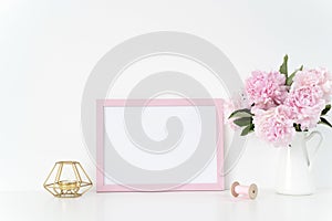 Pink landscape frame mock up with a pink peonies, candle and silk ribbons beside the frame, overlay your quote