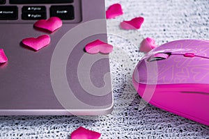 pink laptop keyboard, pink laptop mouse on a light table with scattered hearts