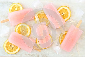 Pink lemonade popsicles with lemon slices on white marble