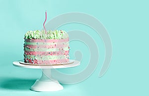 Pink and light blue Birthday sweet cake with colorful sprinkles over a popular light turquoise mint with one party candle on