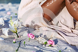 Pink lilies lying on sand foreground and young beatiful woman legs at background on the beach at sunset photo