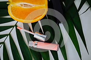 Pink lip gloss lies next to an orange