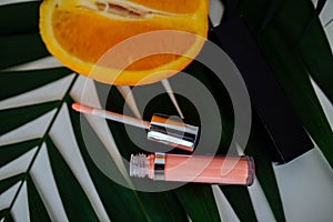 Pink lip gloss lies next to an orange