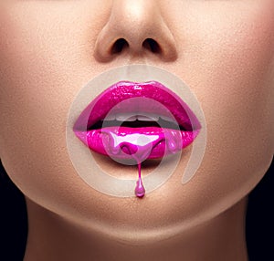 Pink lipstick dripping. Lipgloss dripping from lips, Purple liquid drops on beautiful model girl`s mouth, creative makeup photo