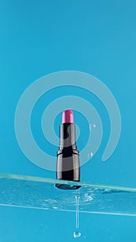 Pink lipstick on a glass shelf on a blue background with drop of water.