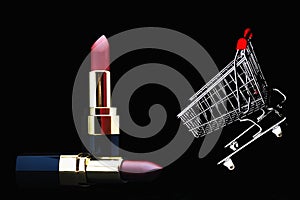 Pink lipstick, gold bars and shopping cart isolated on black background with copy space