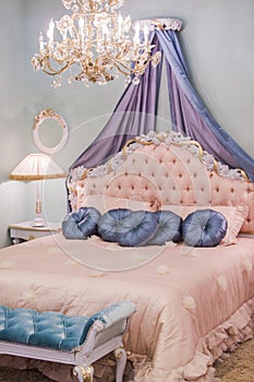 Pink little princess room with satin pillows, bedside lamps, bedside tables, frames on the walls. Luxury rich bedroom interior
