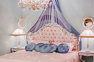 Pink little princess room with satin pillows, bedside lamps, bedside tables, frames on the walls. Luxury rich bedroom interior