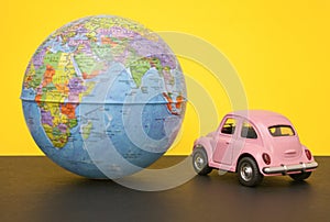 Pink little retro car with world globe sphere. Travel concept. Planning season vacations. Close-up